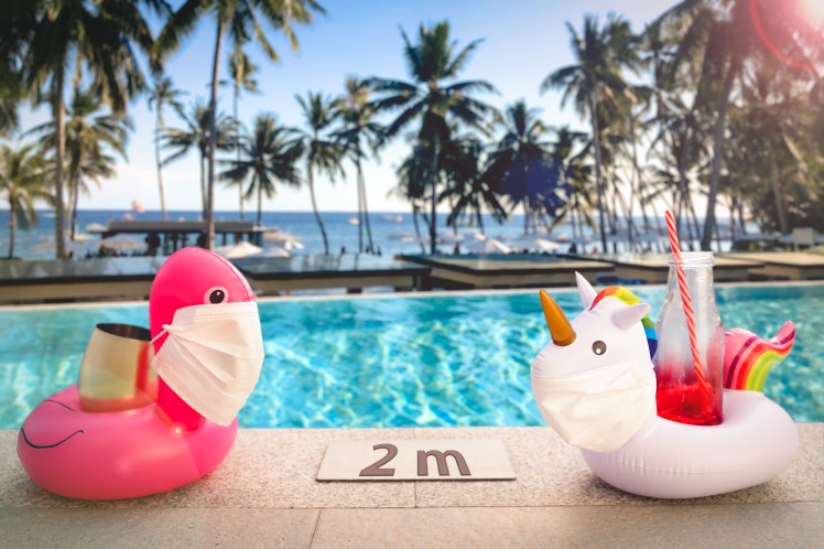 Inflatable pool toys at tropical resort pool wearing face masks staying 2 meters aside to keep social distance during COVID-19 pandemic. Concept of travel industry difficulties during summer 2020